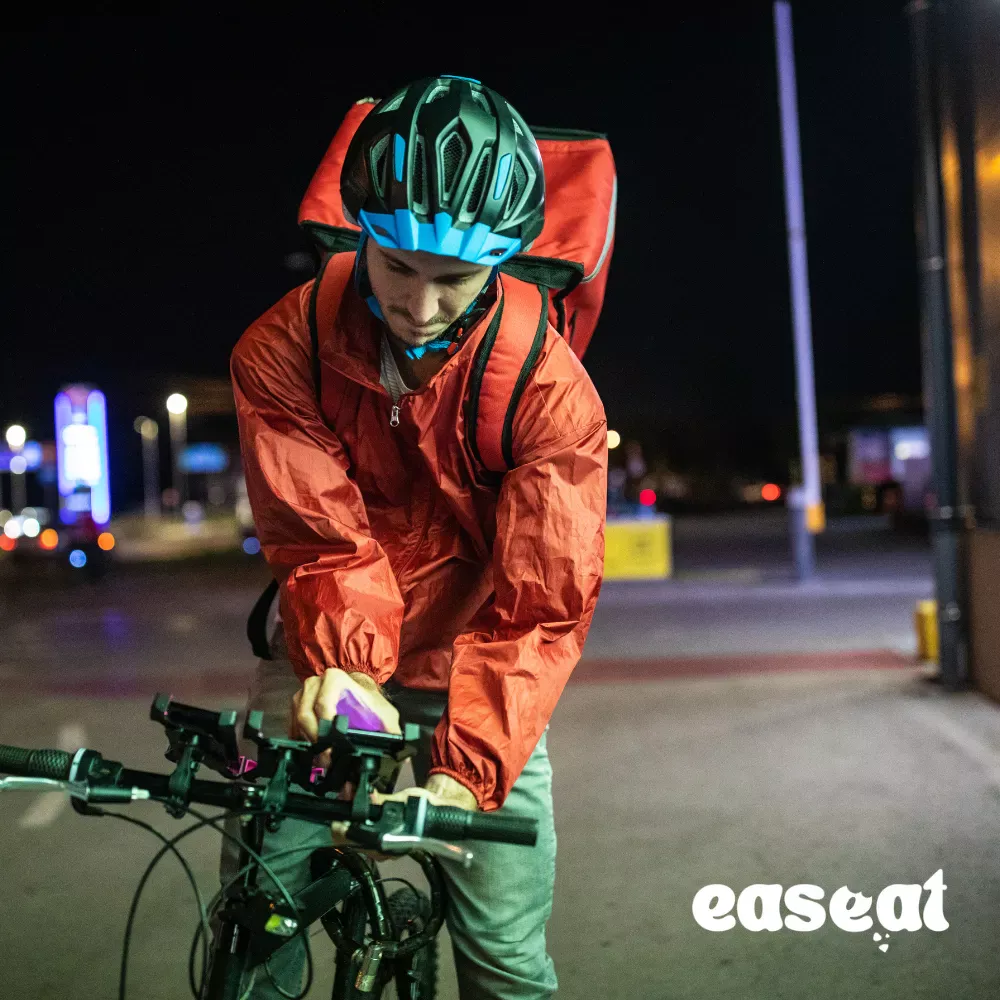 Livreur à vélo consultant son smartphone la nuit – plateforme Easeat de gestion restaurant et click & collect