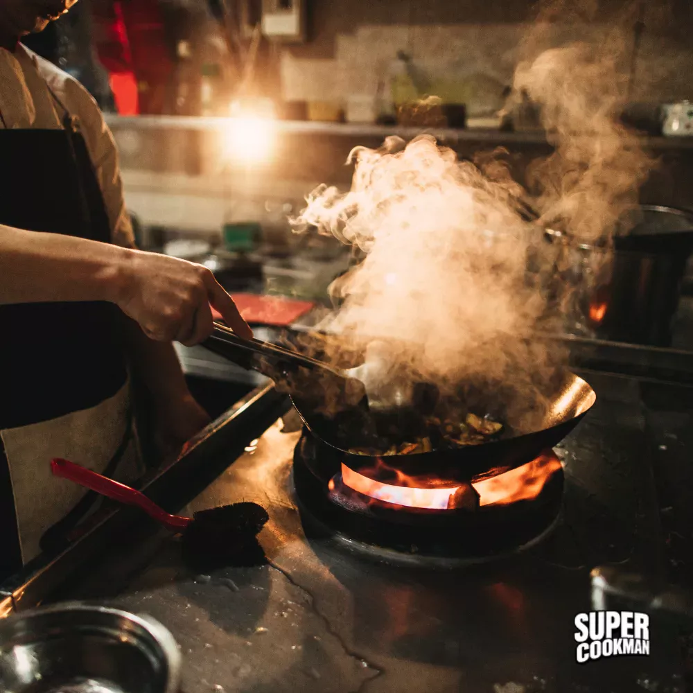 Chef cuisinier en action dans une dark kitchen avec wok enflammé – Supercookman, SaaS de gestion multi-marques développé par YASSITE